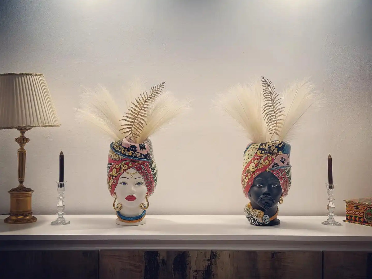 Due vasi decorativi in ceramica a forma di testa con piume e motivi colorati.